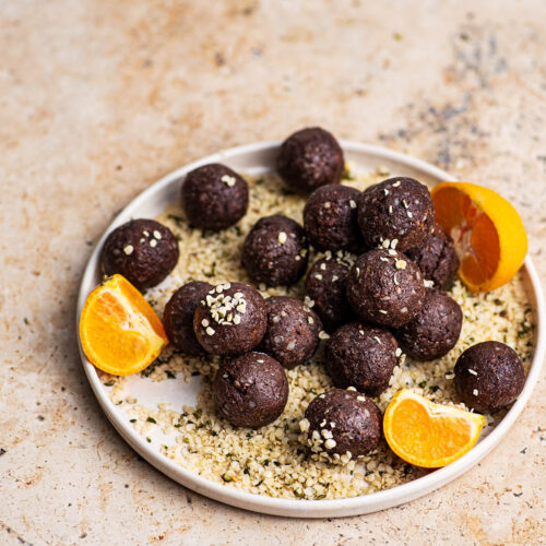 Hemp bites on a plate with more hemp and tangerine pieces.