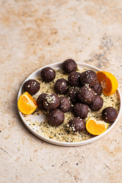 Hemp bites on a plate with more hemp and tangerine pieces.