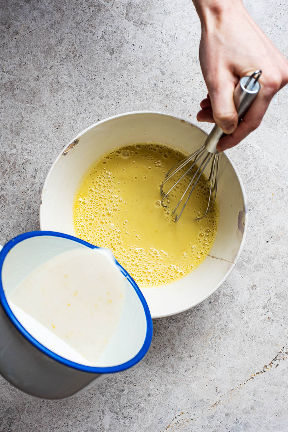 Slowly pouring the cream mixture into the yolks and whisking.