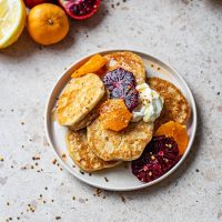 A plate of pancakes with yogurt and orange slices.