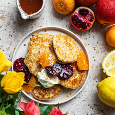 Lemon pancakes on a plate with roses and citrus fruits around.