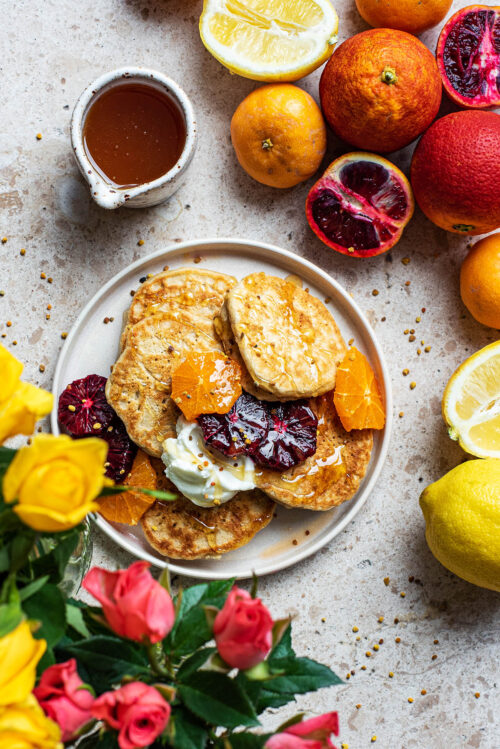 Lemon pancakes on a plate with roses and citrus fruits around.