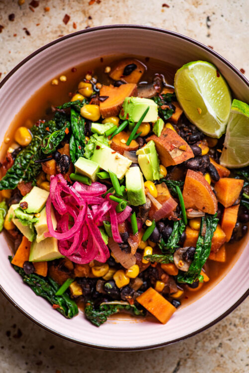 Close up of a bowl of sweet potato chili with avocado and pickled onion.