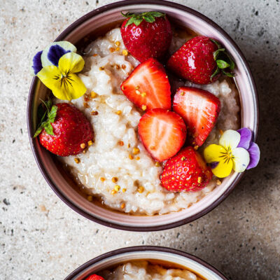 Two bowls of rice pudding, one half in shot, with berries.