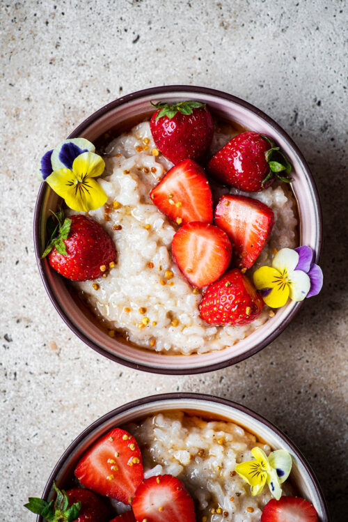 Two bowls of rice pudding, one half in shot, with berries.