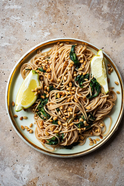 Large plate of spaghetti with spinach, garlic, lemon, and cedar nuts.