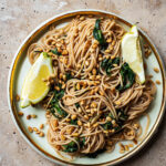 Large plate of spaghetti with spinach, garlic, lemon, and cedar nuts.