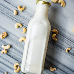 A bottle of cashew milk on its side with cashews around.