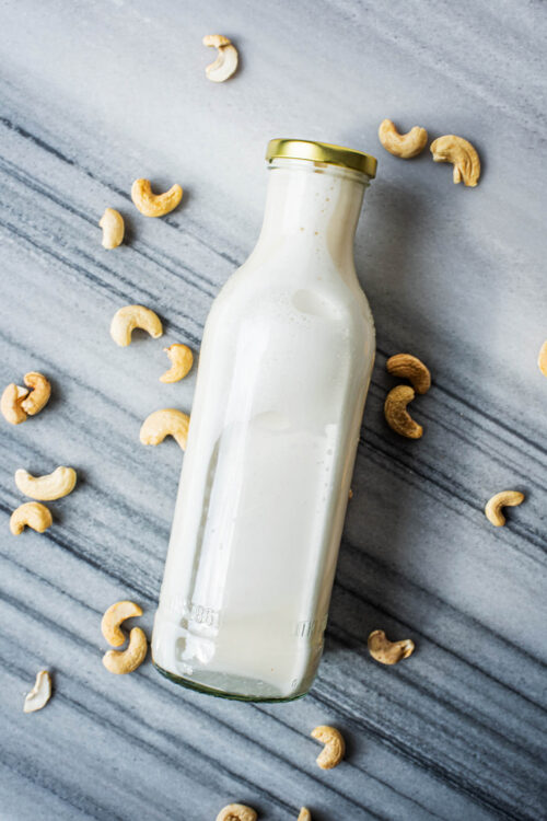 A bottle of cashew milk on its side with cashews around.