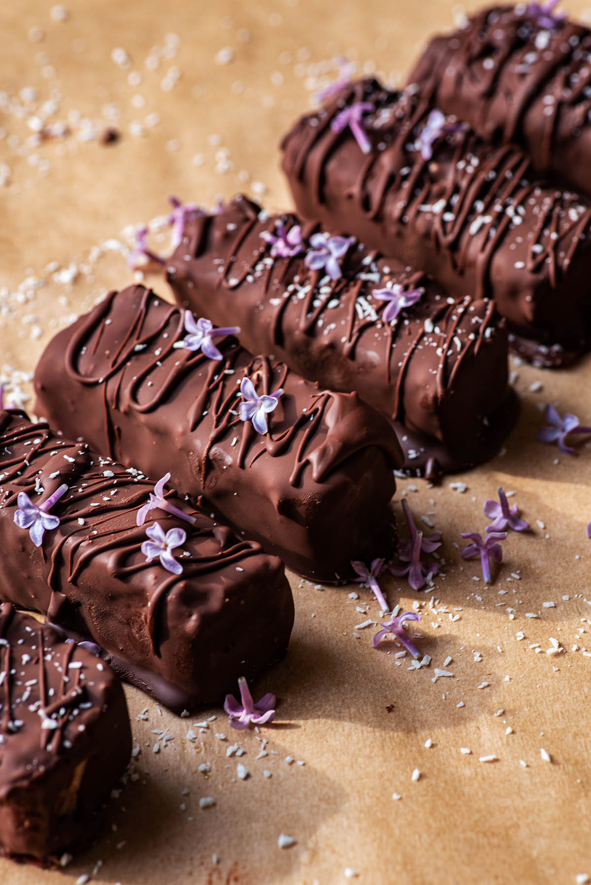 Chocolate coated bars topped with coconut and lilacs in a row.
