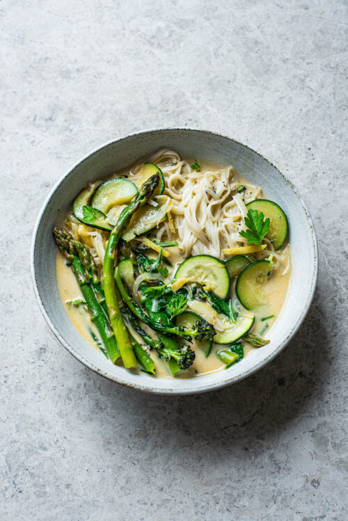 Rice noodles and green vegetables in coconut milk broth.