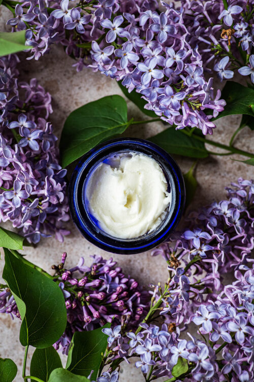 Finished deodorant in a small jar surrounded by lilacs.