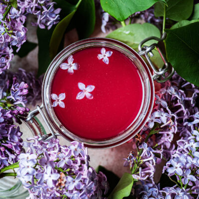 Top down view of glass jar with lilac syrup and blossoms.