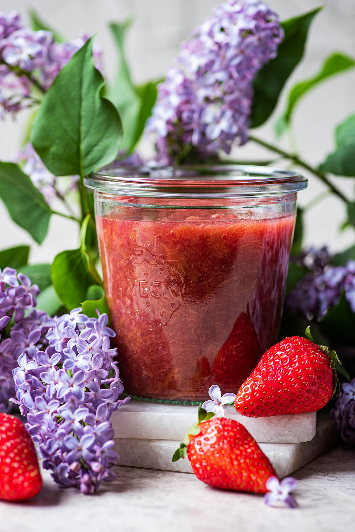 Rhubarb compote in a glass with lilacs and berries.