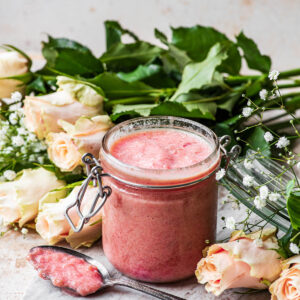 A jar of preserves with a spoon in front and roses around.