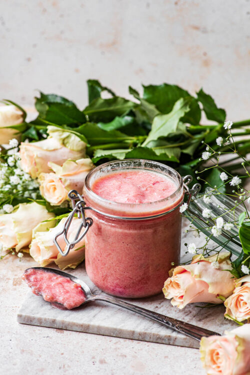 A jar of preserves with a spoon in front and roses around.