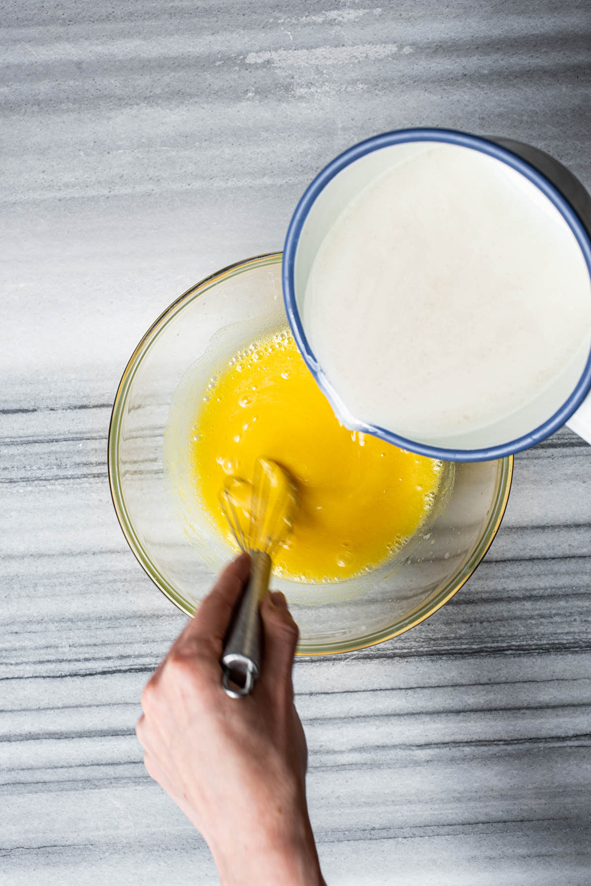 Adding hot milk to egg yolks.
