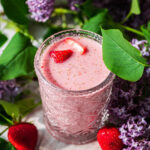 A glass of berry milk with lilacs in background.