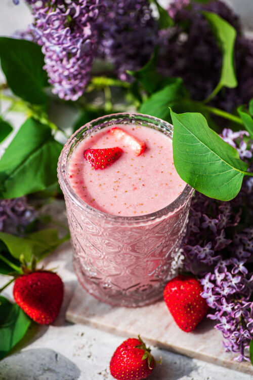 A glass of berry milk with lilacs in background.
