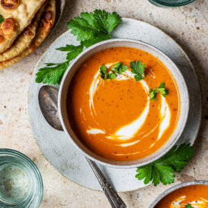 Naan and two bowls of tomato soup with glasses of water.