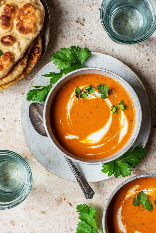 Naan and two bowls of tomato soup with glasses of water.