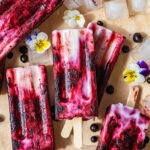 A pile of popsicles with ice, pansies, and wild blueberries around.