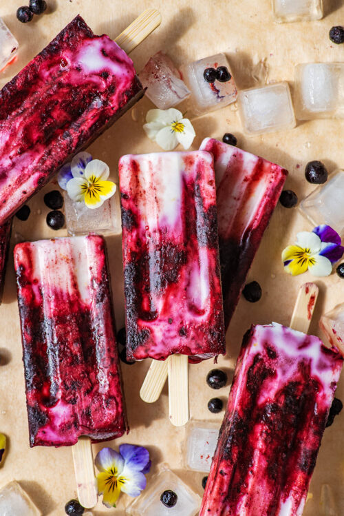 A pile of popsicles with ice, pansies, and wild blueberries around.