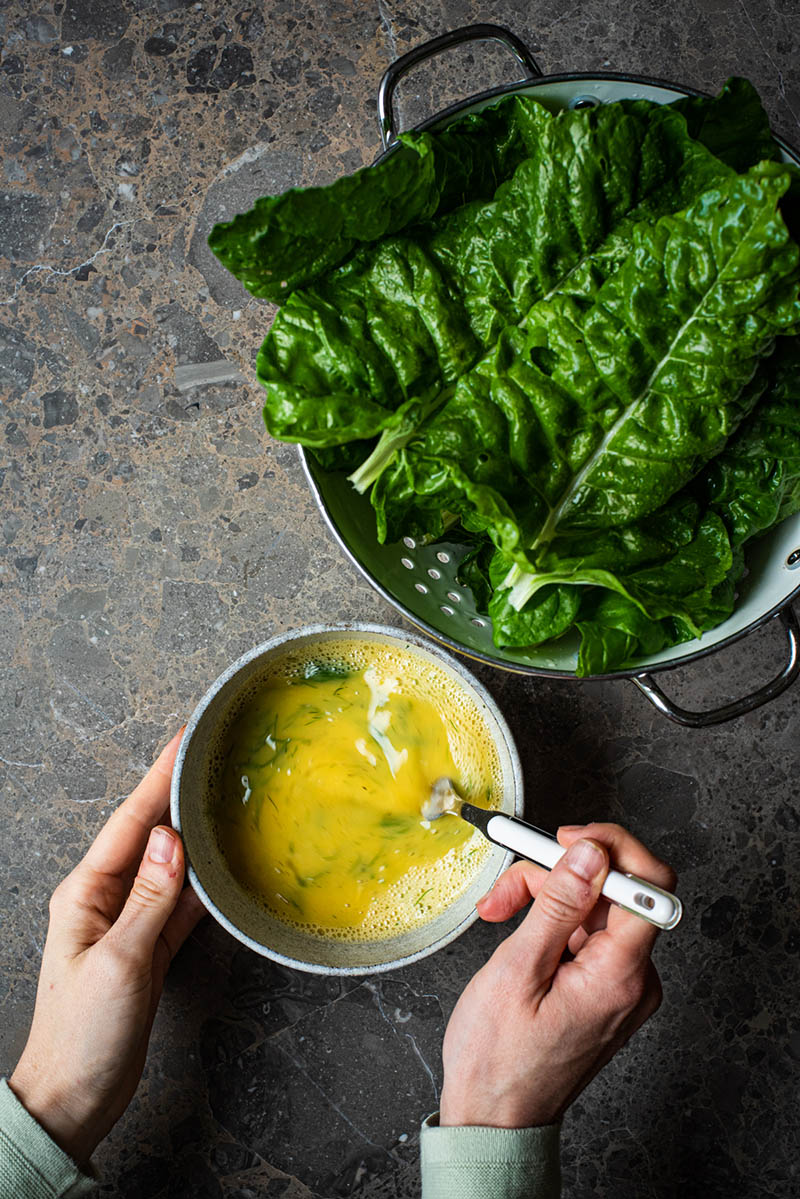 Whisking egg mixture in a bowl with greens in the upper corner.