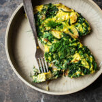 Two pieces of frittata in a deep place with extra herbs and a fork.