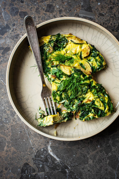 Two pieces of frittata in a deep place with extra herbs and a fork.