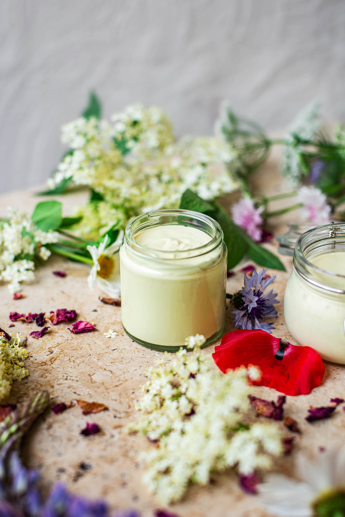 Front view of a glass jar of cream with wildflowers around.
