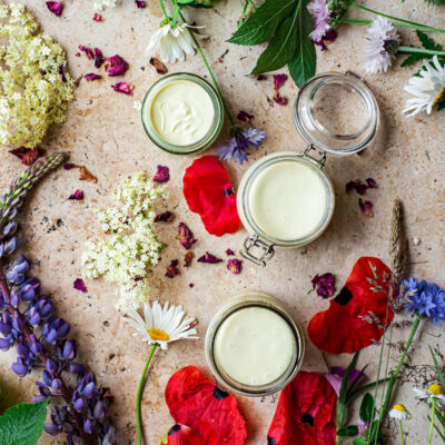 Three small jars of cream surrounded by wildflowers.