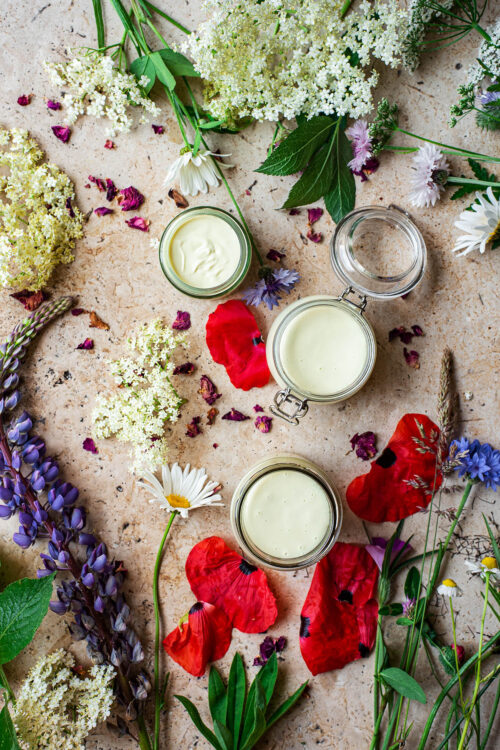 Three small jars of cream surrounded by wildflowers.