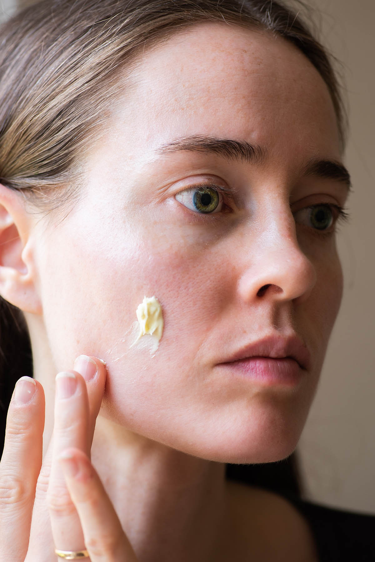 Woman applying face cream to her cheek.