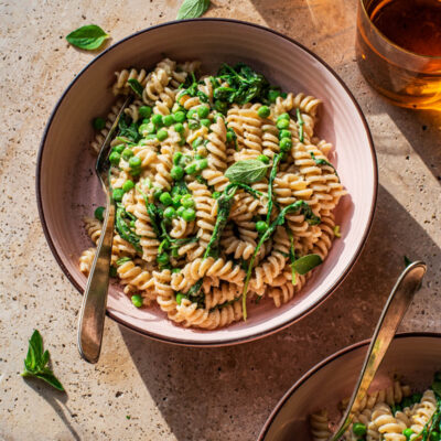 Two bowls of pasta with peas and greens.