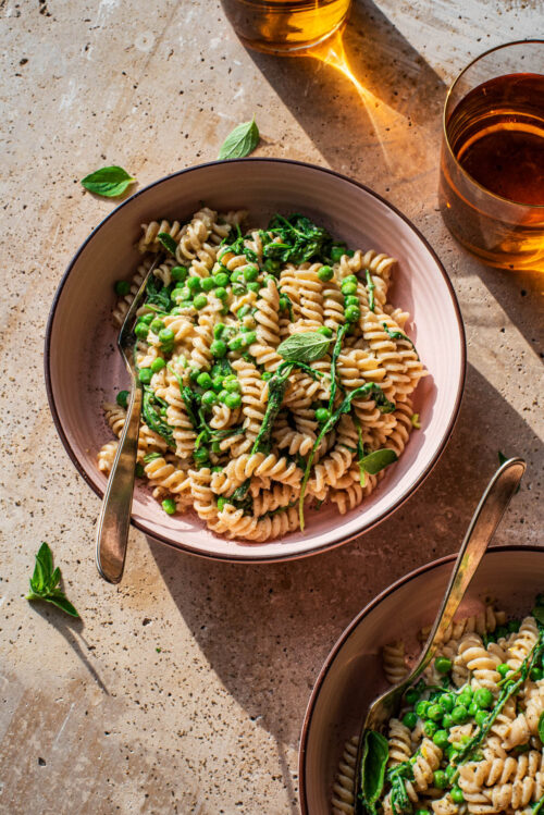 Two bowls of pasta with peas and greens.