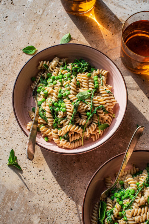 Two bowls of pasta with peas and greens.