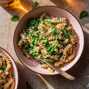 Bowls of hummus pasta with vegetables and two drinks.