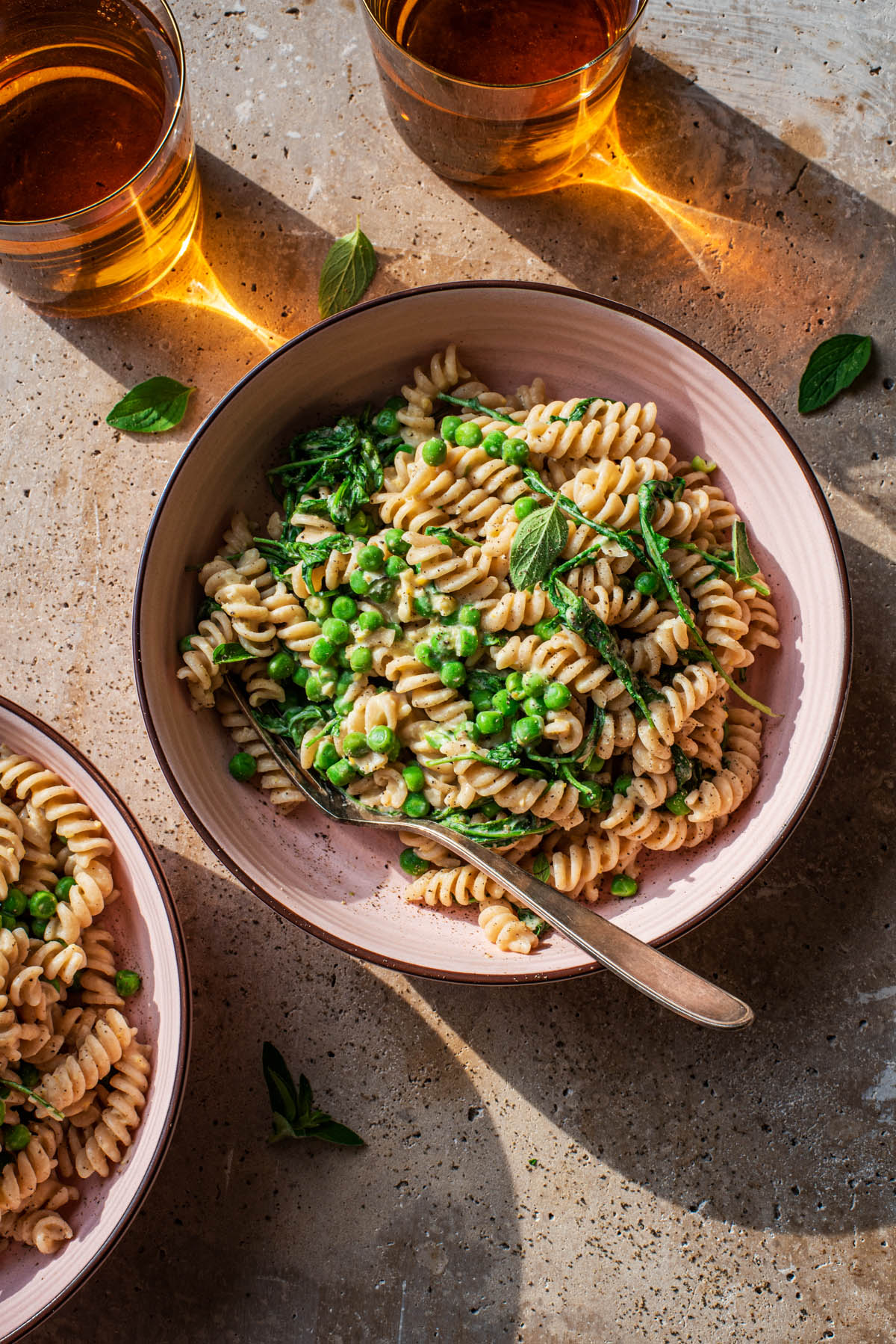 Bowls of hummus pasta with vegetables and two drinks.