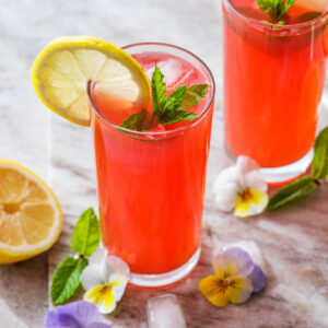 Two glasses of lemonade with lemon slices, mint, and edible flowers.