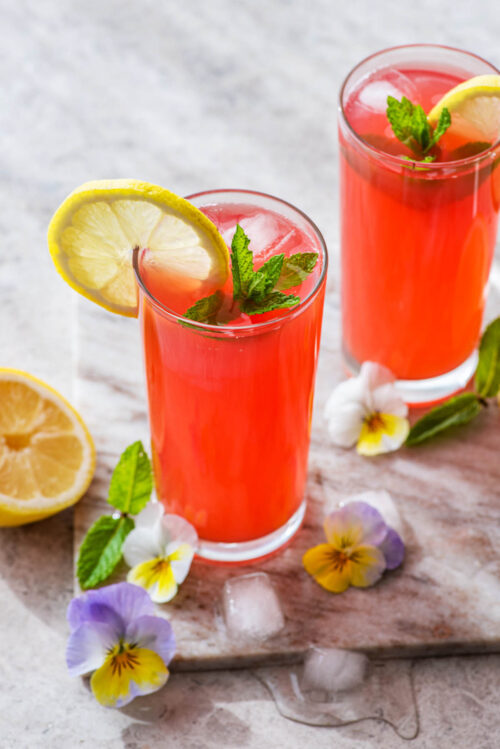 Two glasses of lemonade with lemon slices, mint, and edible flowers.