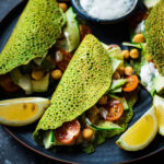 Filled spinach pancakes with lemon wedges and yogurt sauce.