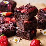 A stack of three brownies with strawberries around.