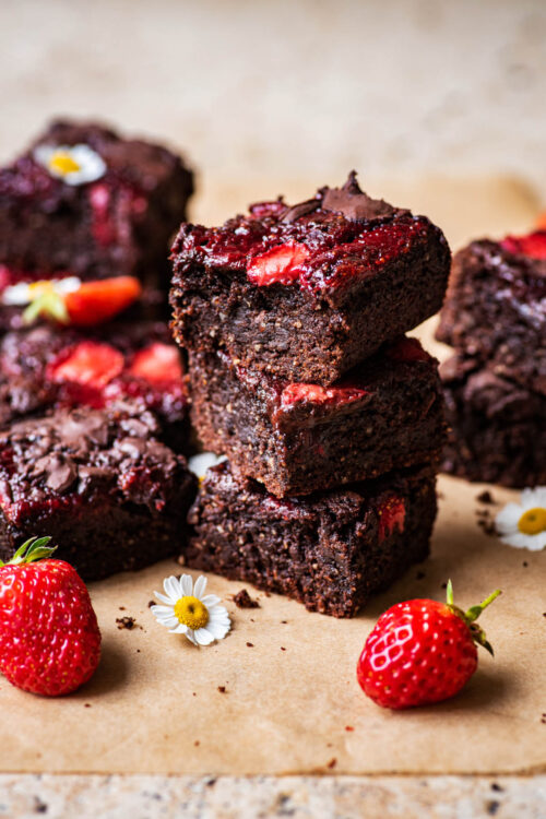A stack of three brownies with strawberries around.