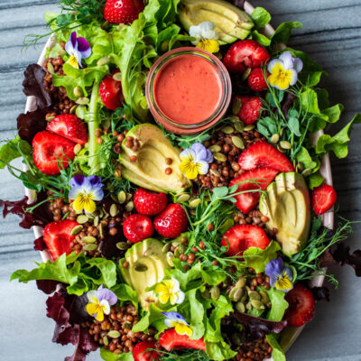 Strawberry salad with edible flowers, avocado, and lentils on a large platter.
