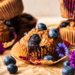 One muffin with paper removed, more stacked in background, with berries around.