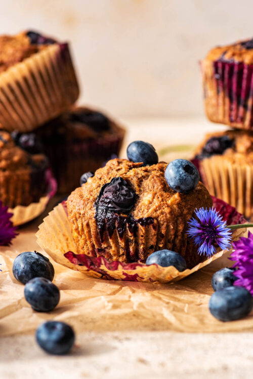 One muffin with paper removed, more stacked in background, with berries around.
