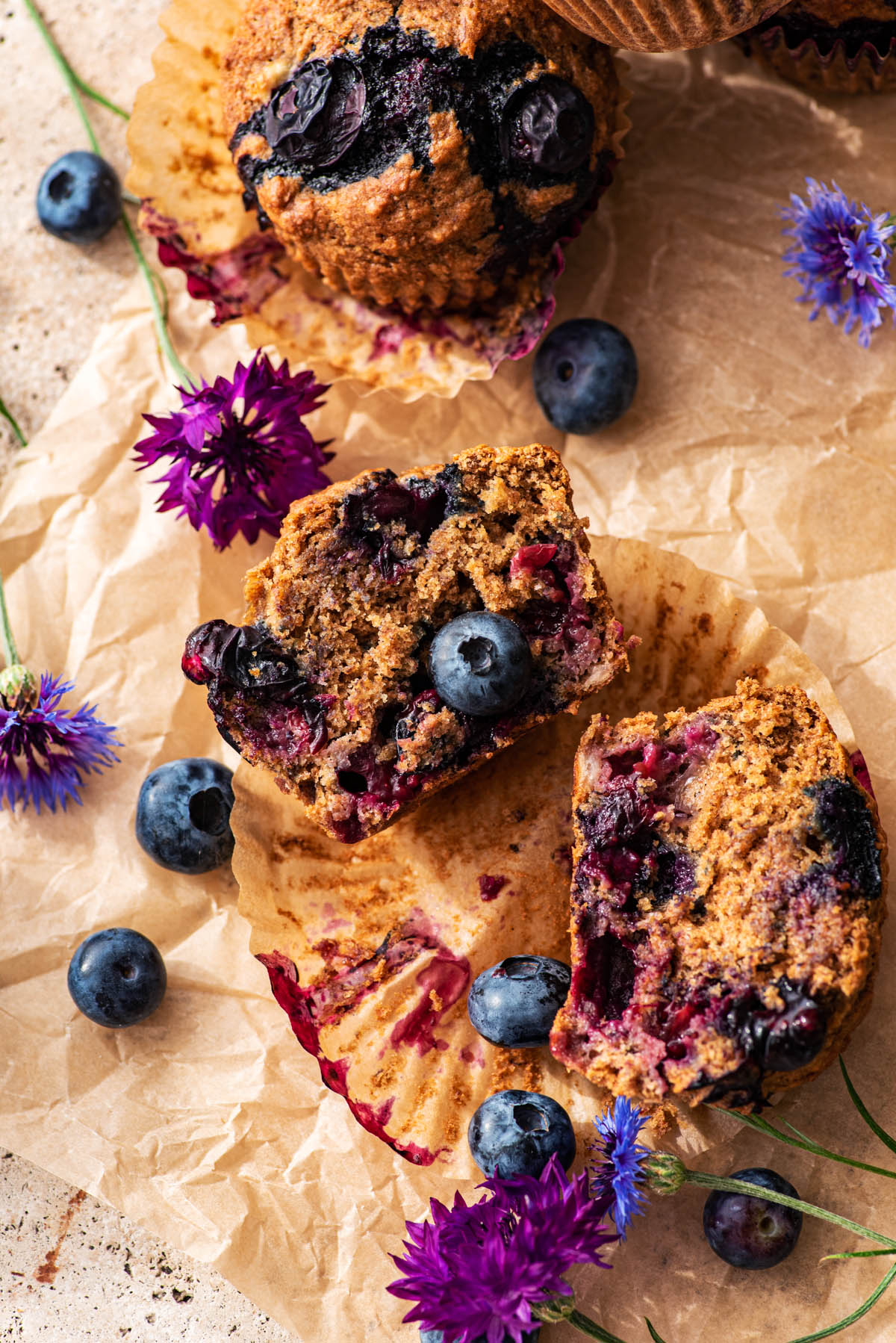 A muffin cut in half with edible flowers and fresh berries around.