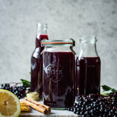 Three glass containers of dark purple elderberry syrup.