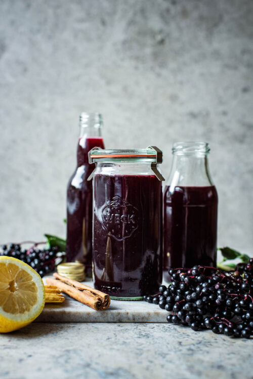 Three glass containers of dark purple elderberry syrup.
